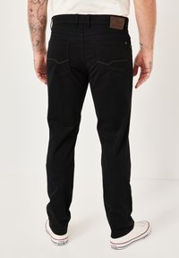 Schwarze gerade geschnittene Hose mit einem Lederetikett auf der Rückseite, ausgestattet mit kontrastierenden Nähten und zwei Gesäßtaschen. Getragen mit weißen Sneakers.