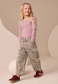 Bluză lavandă cu mâneci lungi, asortată cu pantaloni bej cu imprimeu de leopard negru. Ținuta este completată de două buzunare frontale și adidași vișinii.