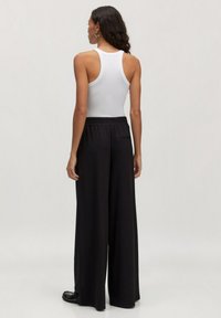 Zwarte wijde broek met een elastische tailleband, gecombineerd met een witte mouwloze top. Gladde stofstructuur, minimalistisch ontwerp.