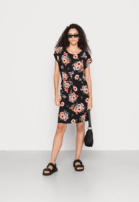 Vestido preto floral com mangas curtas, com flores pink e brancas, silhueta justa e cinto na cintura. Usado com sandálias pretas e bolsa.