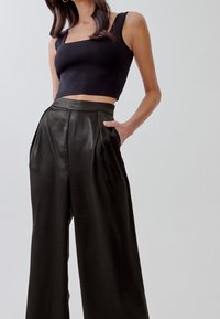 Top corto nero con scollo quadrato, abbinato a pantaloni in pelle a vita alta e gamba larga con pieghe frontali e tasche laterali.