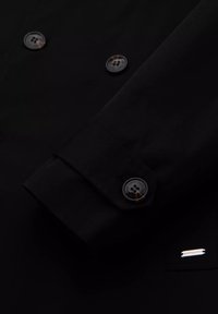 Czarna koszula z guzikami, z błyszczącym wykończeniem, z dwoma okrągłymi guzikami przy mankietach oraz małą metką na kieszeni z przodu.