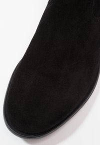 Botín negro de ante hasta el tobillo con punta redonda, textura suave y diseño minimalista. Presenta una suela plana negra y parte superior sin costuras.