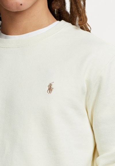 Kermakudonne sweatshirt, joka on valmistettu pehmeästä puuvillasta, ja jossa on pieni ruskeasta langasta brodeerattu polo-logo vasemmassa rintamuksessa. Klassinen pyöreä pääntie.