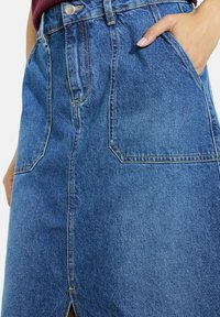 Denim krilo s ravnim krojem, sprednjim razporkom in dvema stranskima žepoma. Ima kontrastne šive in klasičen modri pranje.