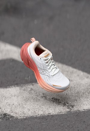 Sapatilha de corrida branca com um upper texturizado, detalhes em rosa e uma sola grossa com um gradiente de rosa para branco. Detalhe do logótipo refletivo.