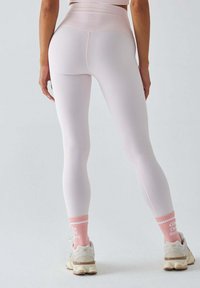 Jasnoróżowe legginsy z wysokim stanem o gładkiej fakturze, uzupełnione różowo-białymi paskowanymi skarpetkami oraz jasnymi, masywnymi sneakersami.