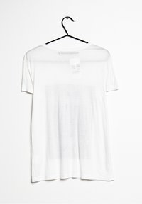 Biała koszulka z krótkim rękawem wyeksponowana na czarnym wieszaku. Wykonana z lekkiego materiału, z okrągłym dekoltem i metką przyszytą z tyłu.