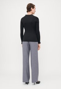 Black long-sleeve top with a ruffled neckline, paired with light gray wide-leg trousers, showcasing a smooth fabric texture and tailored fit.