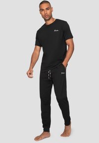 T-shirt noir en coton et joggings assortis. Le T-shirt a un col rond et un petit logo blanc ; les joggings sont dotés d'une taille élastique et de poches.