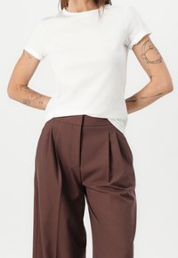 Weißes Baumwoll-T-Shirt mit umgeschlagenen kurzen Ärmeln, kombiniert mit braunen, gefalteten Hosen mit hoher Taille und weiter Beinform.