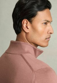 Pullover con colletto e maniche lunghe in tessuto rosa chiaro. Presenta un colletto alto, una texture liscia e un design aderente senza motivi visibili.