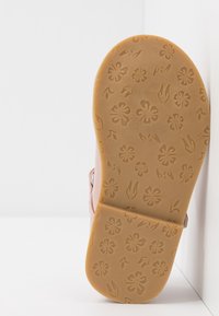 Sandalia de color rosa claro con suela de goma que presenta un patrón de flores en relieve, textura suave y un diseño de tira simple.