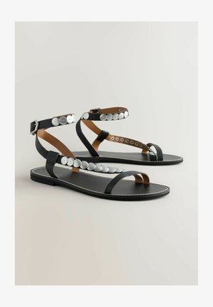 Sandales plates noires avec une finition en cuir lisse, dotées d'accents en bouton argenté le long des sangles et d'un design minimaliste.