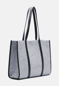 Grå tote-väska i filt med svarta läderdetaljer och remmar, med vertikala sömmar och öppen toppdesign.