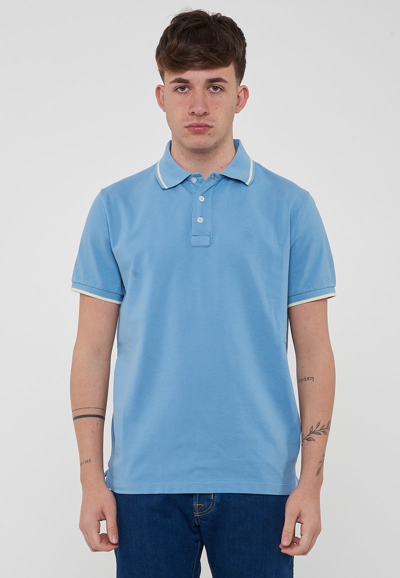 Polo shirt azzurro chiaro con colletto e bordo delle maniche bianchi a contrasto. Presenta una chiusura a tre bottoni e un dettaglio del logo sul lato sinistro del petto.