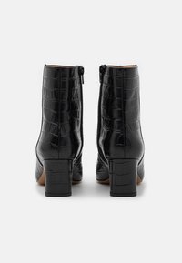 Botas negras hasta el tobillo de cuero con relieve de coco, con tacón de forma cuadrada y cremallera lateral, que presentan una textura suave y acentos mínimos.