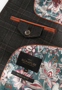 Tissu de veste en tartan sombre avec des accents marron, présentant une doublure florale dans des tons de bleu sarcelle, rose et crème. Comprend un détail de poche boutonnée.
