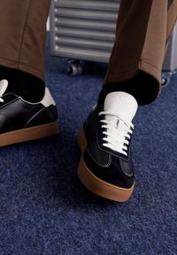 Black and white sneakers with a smooth leather upper, white laces, and a gum rubber sole, featuring contrasting stitching details.