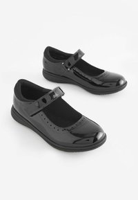 Zapatos Mary Jane de charol negro con una banda de Velcro, puntera redondeada, interior acolchado y perforaciones decorativas en la parte frontal.