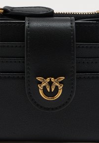 Crna kožna novčanik s teksturiranim završetkom, koji ima zlatni simbol ptice i zatvaranje na preklop, naglašen rajsferšlusom i šivanim rubovima.