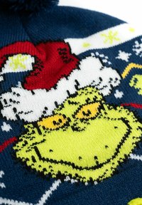 Berretto lavorato a maglia con il Grinch di un vivace verde, un cappello da Babbo Natale rosso, dettagli neri e uno sfondo blu con fiocchi di neve bianchi e motivi.
