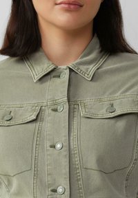 Olivgrüne Denimjacke mit Knopfverschluss, zwei Brusttaschen und auffälligen Steppdetails. Weiche Textur mit strukturiertem Schnitt.