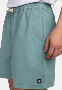 Svetle modré šortky vyrobené z bavlny, s elastickým pasem a šňůrkou, bočními kapsami a malou značkovou etiketu na lemu.