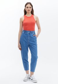 Červený bezrukávový top, světle modré džíny s vysokým pasem a nařaseným páskem, a bílé tenisky s šedými a černými akcenty.