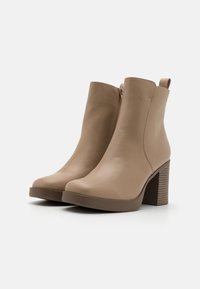 Botines de cuero beige con acabado liso, con cremallera lateral y un tacón alto apilado con un detalle a rayas.