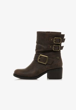 Braune Lederstiefel in Schafthöhe mit drei messingfarbenen Schnallen und einem niedrigen, gestapelten Blockabsatz, von der Außenseite auf einem weißen Hintergrund dargestellt.