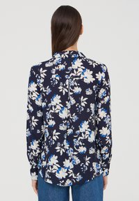 Camicetta floreale in blu navy con fiori bianchi e blu, maniche lunghe, colletto e piega posteriore. Tessuto morbido, design casual e orlo arrotondato.