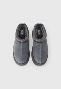 Par sivi od antilopa UGG papuča na slip-on s crnim gumenim potplatom i mekanim флисом, prikazane odozgo na bijeloj pozadini.