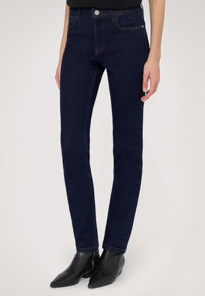 Donkerblauwe skinny jeans van denim met een gladde textuur, vijf zakken en contrasterende rode stiksels. Combinatie met puntige zwarte enkellaarsjes.