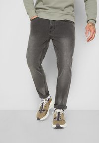 Jeans de mezclilla gris con corte ajustado, textura desgastada y diseño de cinco bolsillos, combinados con zapatillas deportivas en beige y blanco.