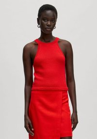 Red knitted sleeveless top with a textured finish and a high neckline, paired with a matching fitted skirt. Simple, clean design.