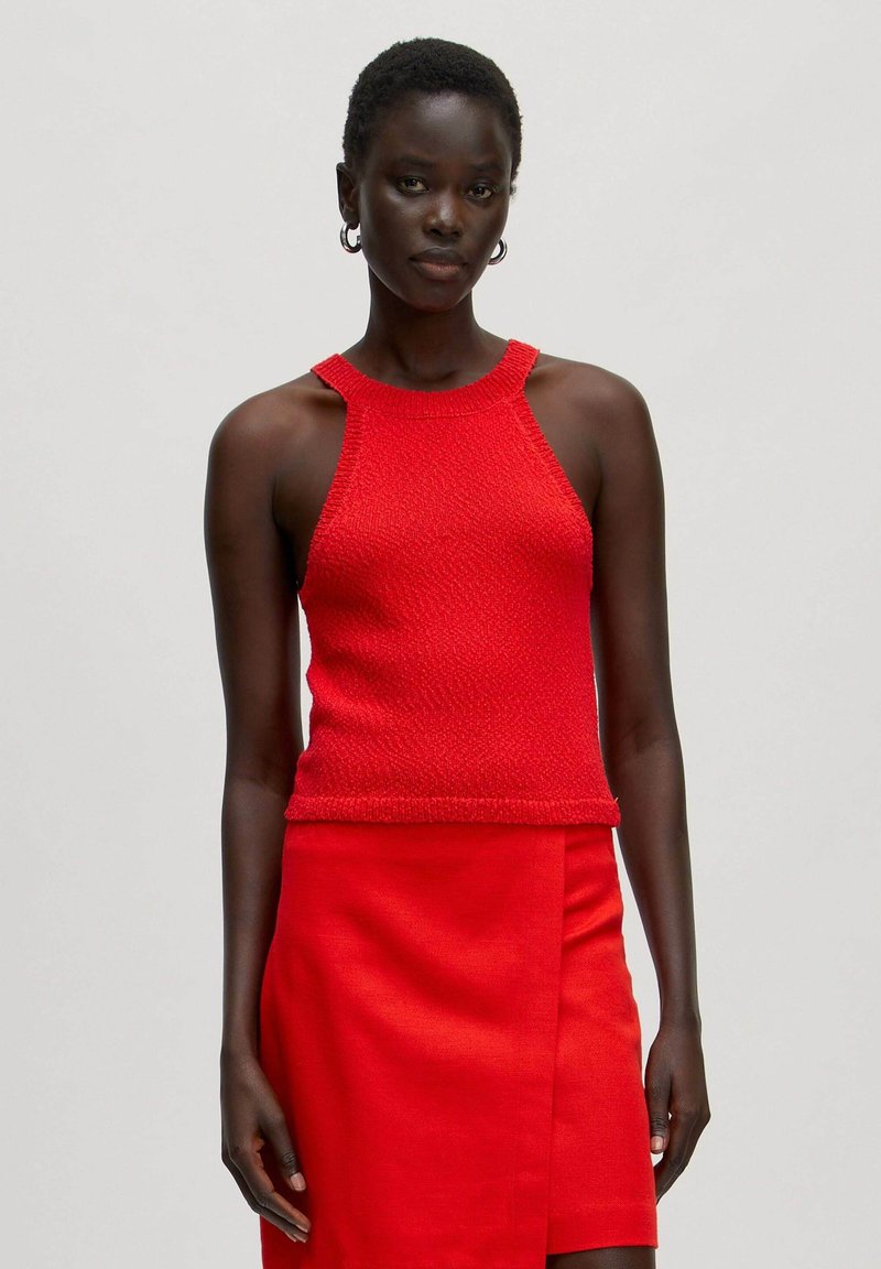 Red knitted sleeveless top with a textured finish and a high neckline, paired with a matching fitted skirt. Simple, clean design.