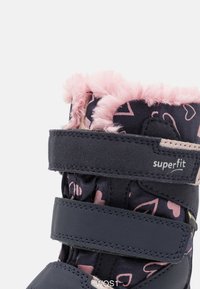 Stivale invernale nero e rosa con morbida bordatura in finta pelliccia rosa, motivo a cuori sulla parte superiore e due cinturini in velcro regolabili.