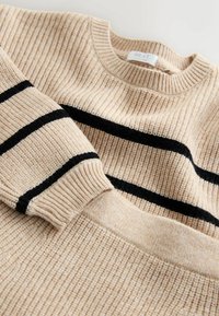 Beige ribstrikket sweater med sorte vandrette striber. Strikket tekstur, rund halsudskæring og mærkevisning ved kraven.