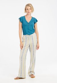 Teal T-shirt met korte mouwen en knopen, gecombineerd met lichtgekleurde gestreepte broek met blauwe en gele lijnen, en platte sandalen.