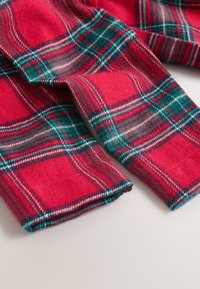 Tissu écossais rouge et vert avec une texture douce. Partiellement plié, mettant en valeur le motif et les détails de l'ourlet. Convient pour les vêtements.