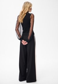 Czarna bluzka z przezroczystymi, grochy pufkami i dopasowanym fasonem. Czarne szerokie spodnie z kontrastowym, pionowym beżowym paskiem.