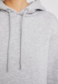 Sweat à capuche gris avec cordons et œillets en métal ; fabriqué en tissu doux et texturé ; doté d'une coupe décontractée et d'une grande capuche.