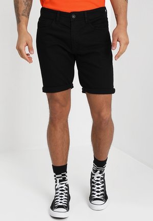 Shorts en jean noir avec un ourlet retroussé, design à cinq poches et fermeture à bouton, associés à des baskets montantes noir et blanc et des chaussettes rayées.