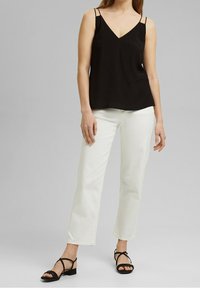 Top nero con spalline sottili e scollo a V, abbinato a jeans bianchi a gamba dritta e sandali neri con cinturini. Tessuto morbido, vestibilità comoda.