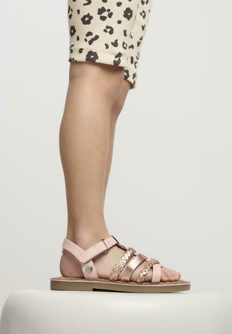 Sandalía rosa y dorada metálica con múltiples correas, cierre de hebilla, suela plana y plantilla texturizada, situada sobre una superficie blanca.