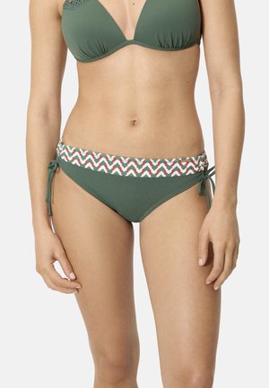 Mujer con bikini verde oliva con cinturilla estampada y lazos laterales en la parte inferior del bikini, posando contra un fondo liso.