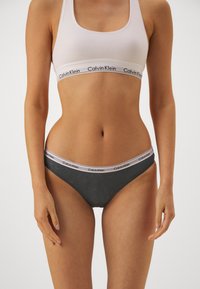 Calvin Klein melltartó és tangapánt szett. Fehér pamut melltartó logós pánttal. Szürke csipke tangapánt, amelyhez illő logós derékpánt tartozik. Puha tapintás.