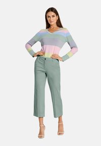 Gestreepte V-hals trui in pastelkleuren, gecombineerd met hooggewaisted, lichtgroene wijde broek. Het model draagt enkelsandalen.