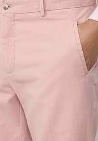 Pantaloni in cotone rosa chiaro con tasca laterale e chiusura con bottone, caratterizzati da una texture liscia e un design pulito.